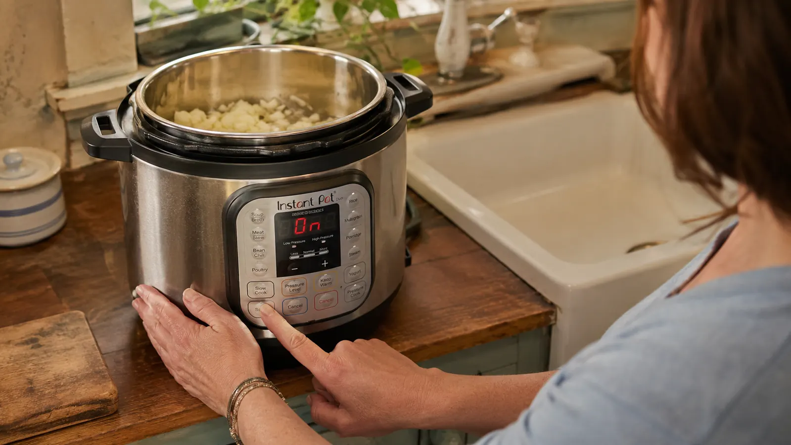 A hand pressing the sauté button on an Instant Pot Duo with onions cooking inside