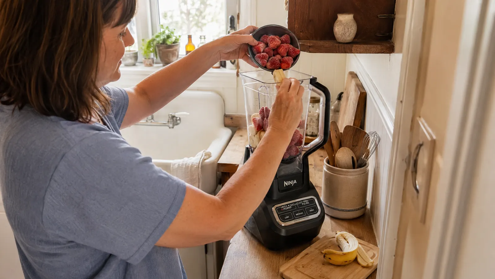 Hands loading frozen fruit into the Ninja Mega Kitchen System pitcher